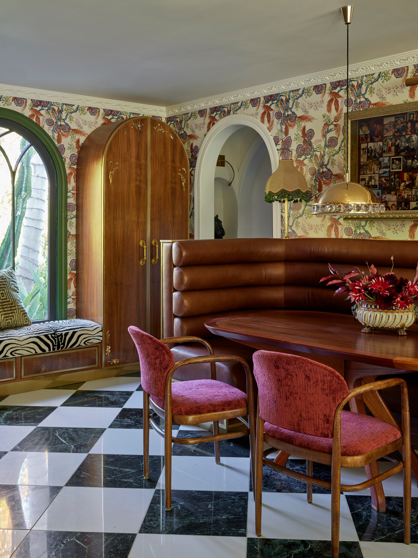 Studio Nauleau breakfast nook with a curved banquette, floral wallpaper, checkerboard floor, and pink dining chairs