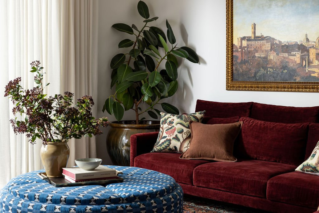 Warm living room with a deep red sofa and layered textiles by Studio Nauleau